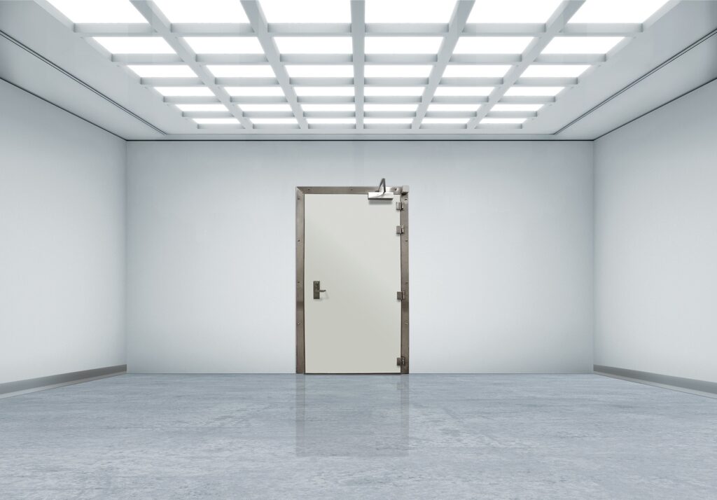 White industrial room with grid ceiling lights and a centered metal door